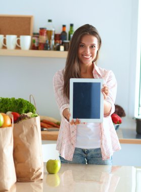 Mutfakta yemek yapmak için tablet bilgisayar kullanan genç bir kadın.