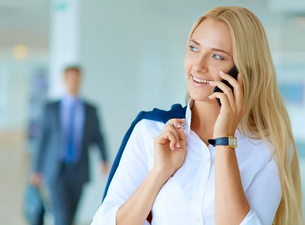 Businesswoman standing against office window talking on mobile phone — Stock Photo, Image