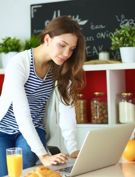 Attraktiv ung kvinna med laptop och sitter i köket — Stockfoto