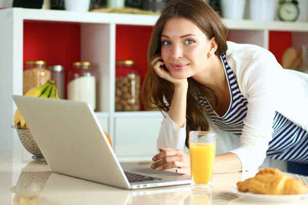 Attraktiv ung kvinna med laptop och sitter i köket — Stockfoto