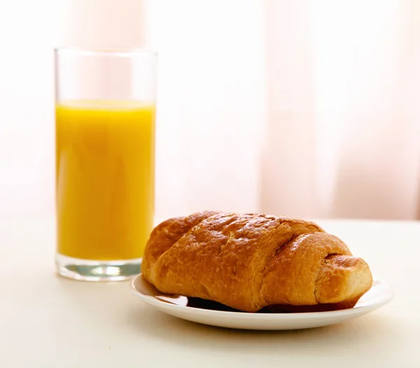 Glass of juice and croissant on a plate — Stock Photo, Image