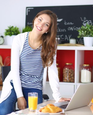 Dizüstü bilgisayar kullanarak ve mutfakta oturmuş çekici genç kadın