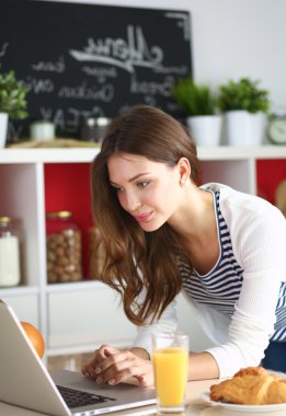 Dizüstü bilgisayar kullanarak ve mutfakta oturmuş çekici genç kadın