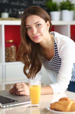 Dizüstü bilgisayar kullanarak ve mutfakta oturmuş çekici genç kadın