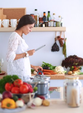 Mutfakta yemek yapmak için tablet bilgisayar kullanan genç bir kadın.