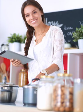 Mutfakta yemek yapmak için tablet bilgisayar kullanan genç bir kadın.