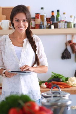 Mutfakta yemek yapmak için tablet bilgisayar kullanan genç bir kadın.