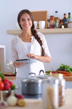 Mutfakta yemek yapmak için tablet bilgisayar kullanan genç bir kadın.