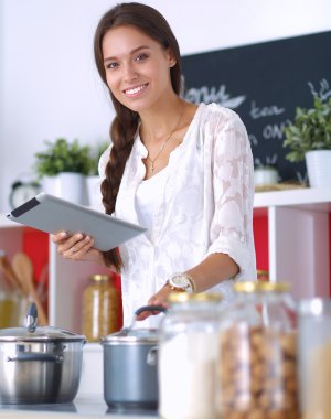 Mutfakta yemek yapmak için tablet bilgisayar kullanan genç bir kadın.