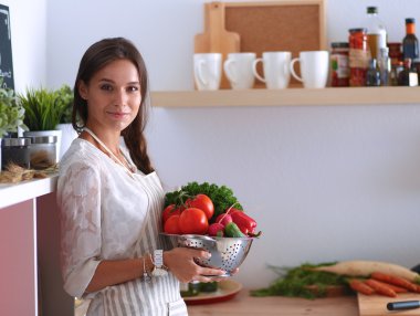 Mutfakta elinde sebzelerle gülümseyen genç bir kadın.