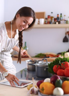 Mutfakta yemek yapmak için tablet bilgisayar kullanan genç bir kadın.