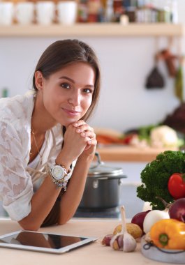 Mutfakta yemek yapmak için tablet bilgisayar kullanan genç bir kadın.