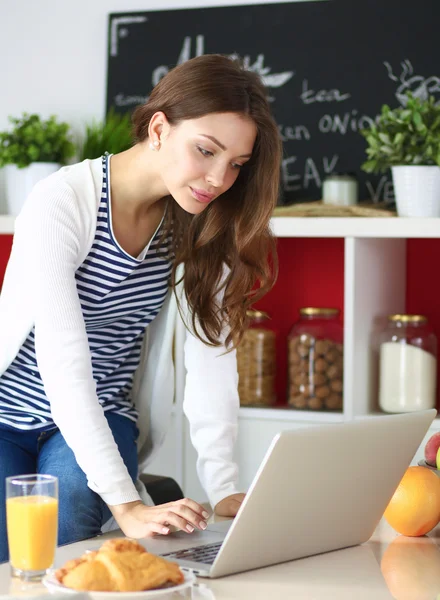 Mujer joven atractiva usando el ordenador portátil y sentado en la cocina — Foto de Stock