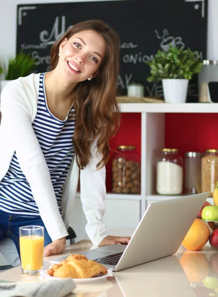 Atrakcyjna młoda kobieta za pomocą laptopa i siedzi w kuchni — Zdjęcie stockowe