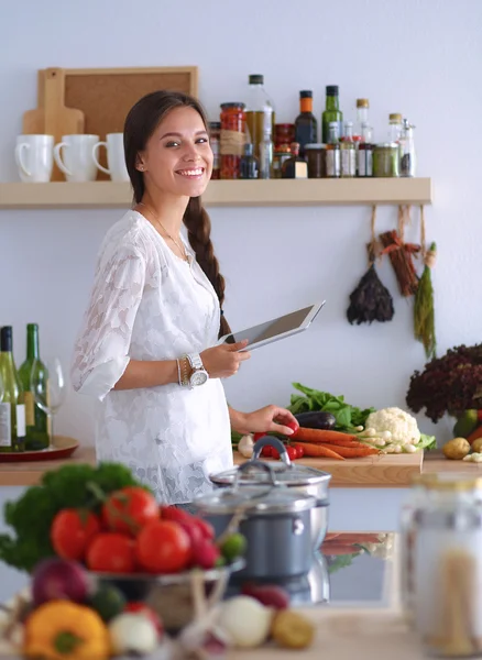 Mutfakta yemek yapmak için tablet bilgisayar kullanan genç bir kadın.