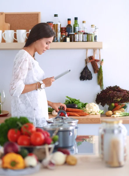 Mutfakta yemek yapmak için tablet bilgisayar kullanan genç bir kadın.