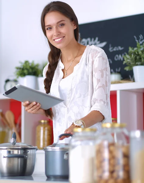 Mutfakta yemek yapmak için tablet bilgisayar kullanan genç bir kadın.