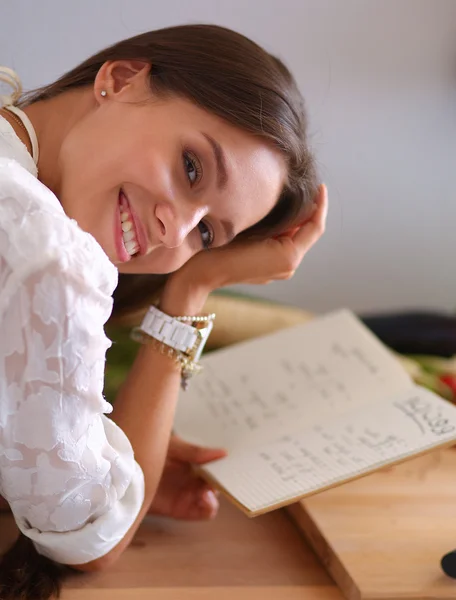 Jovem mulher lendo livro de receitas na cozinha, à procura de receita — Fotografia de Stock