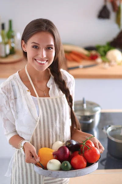 Glimlachende jonge vrouw met groenten in de keuken — Stockfoto