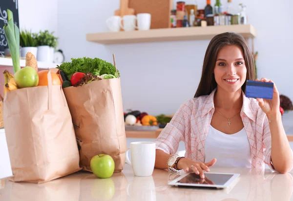 Usmívající se žena online nakupování pomocí tabletu a kreditních karet v kuchyni — Stock fotografie