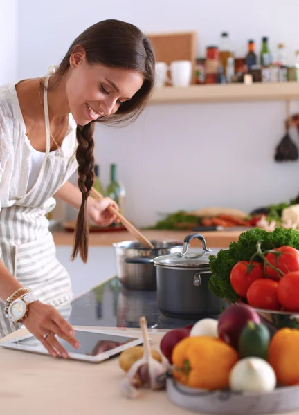 Jovem usando um computador tablet para cozinhar em sua cozinha — Fotografia de Stock