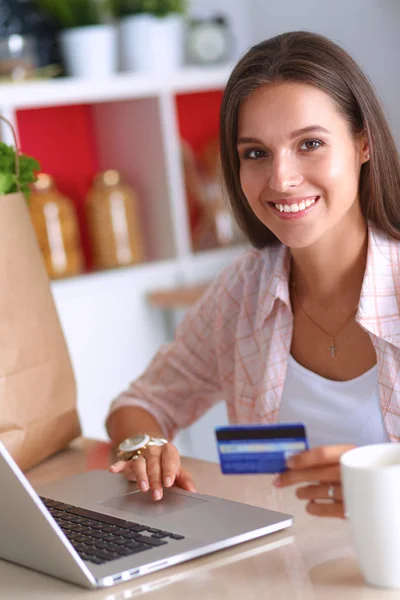 Mujer sonriente compras en línea utilizando la tableta y la tarjeta de crédito en la cocina —  Fotos de Stock