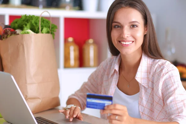 Mujer sonriente compras en línea utilizando la tableta y la tarjeta de crédito en la cocina —  Fotos de Stock