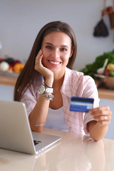 Улыбающаяся женщина онлайн покупки с помощью планшета и кредитной карты на кухне — стоковое фото