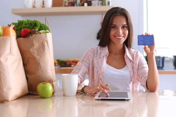 Femme souriante achats en ligne en utilisant tablette et carte de crédit dans la cuisine — Photo