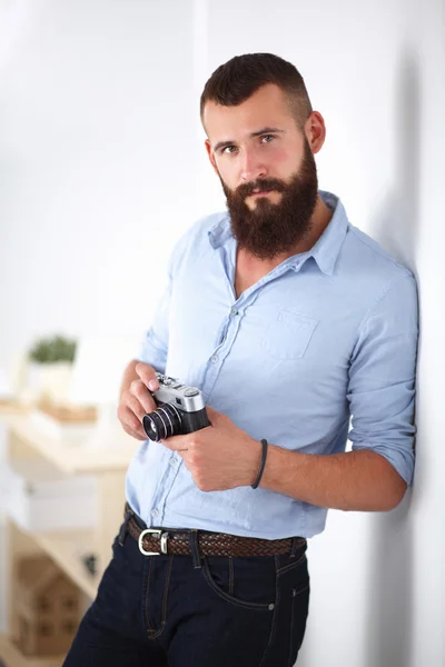 Junger Mann mit Bart hält eine Kamera während er vor weißem Hintergrund steht — Stockfoto