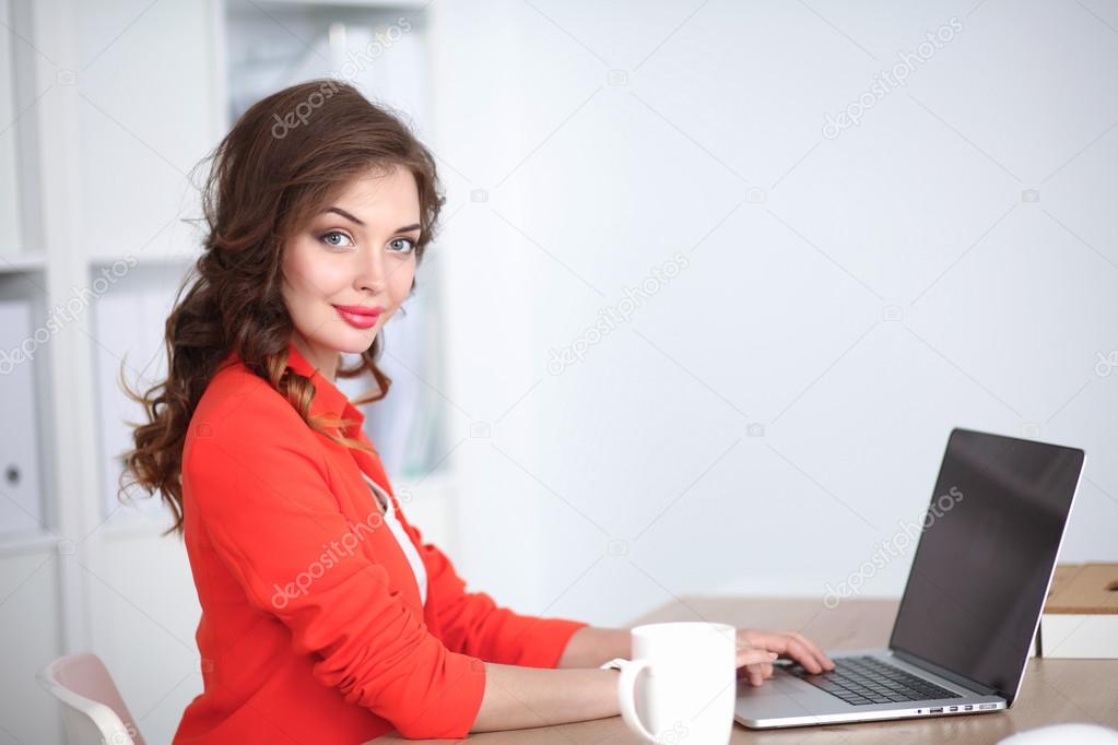 Attractive woman sitting at desk in office, working with laptop computer
