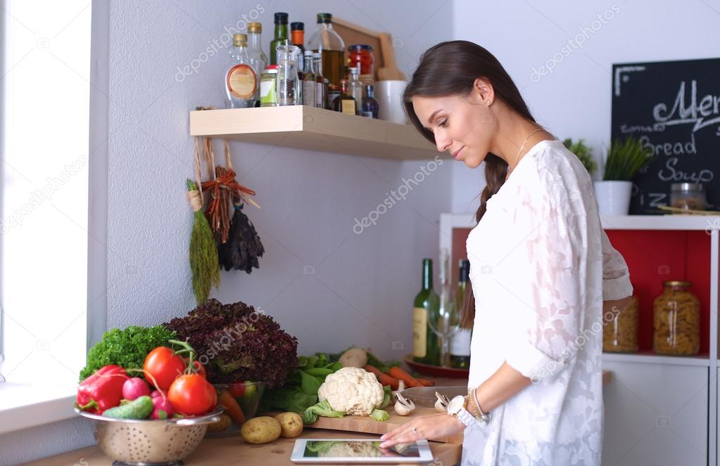 Young woman using a tablet computer to cook in her kitchen