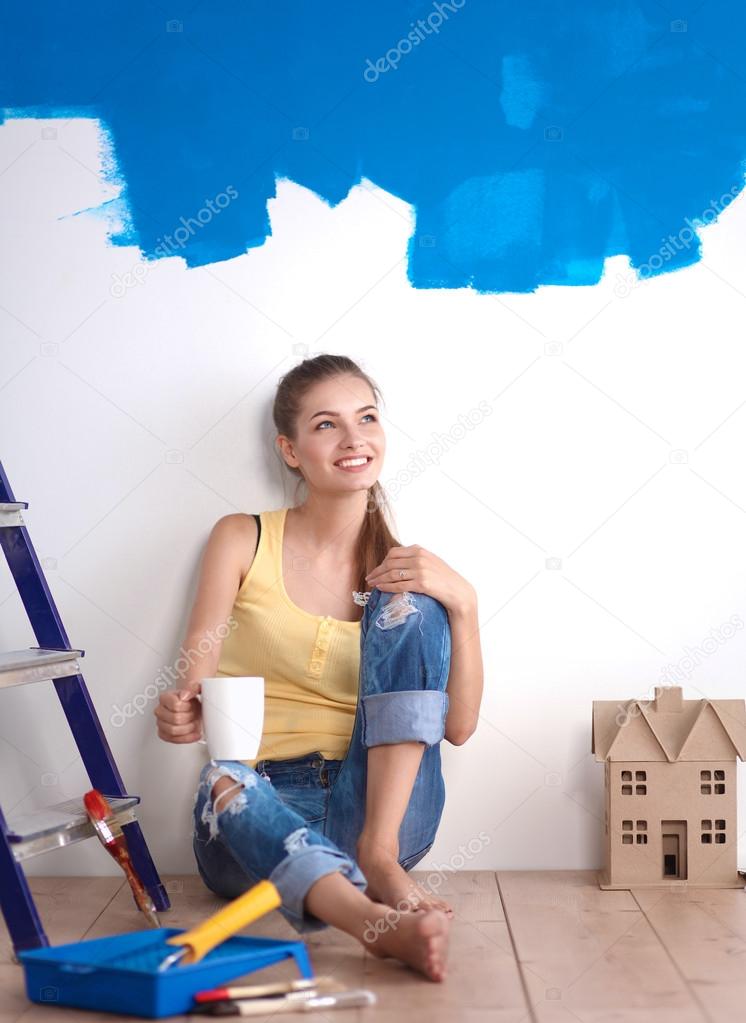 Portrait of female painter sitting on floor near wall after painting.