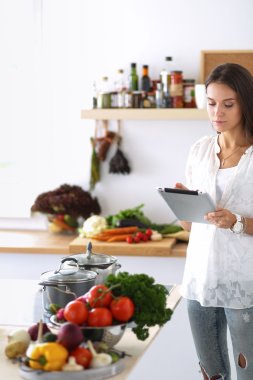 Mutfakta yemek yapmak için tablet bilgisayar kullanan genç bir kadın.