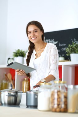 Mutfakta yemek yapmak için tablet bilgisayar kullanan genç bir kadın.