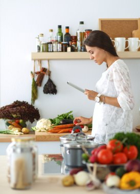 Mutfakta yemek yapmak için tablet bilgisayar kullanan genç bir kadın.