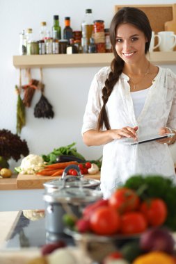 Mutfakta yemek yapmak için tablet bilgisayar kullanan genç bir kadın.