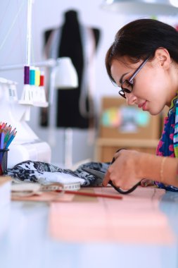 Moda tasarımcısı dikiş makinesinin yanında tekstil kesiyor.