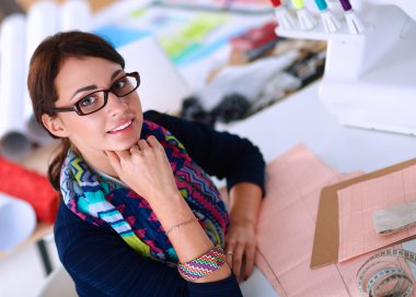 Güzel moda tasarımcısı stüdyoda masada oturuyor.