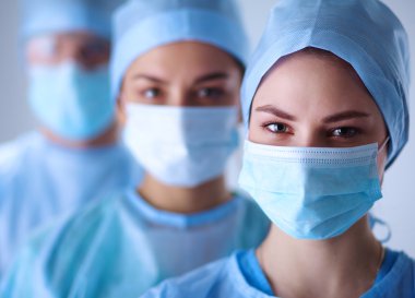 Cerrahlar, koruyucu üniformalar, kepler ve maskeler giyiyorlar.