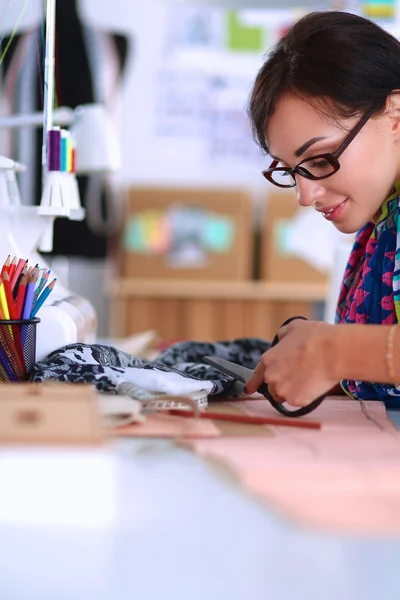 Fashion designer cutting textile next to a sewing machine — Stock Photo, Image