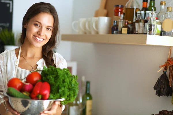 Souriante jeune femme tenant des légumes debout dans la cuisine — Photo