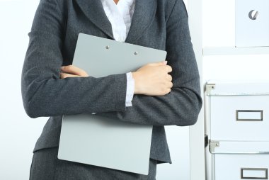 Çekici genç iş kadını masanın yanında elinde dosyayla duruyor.