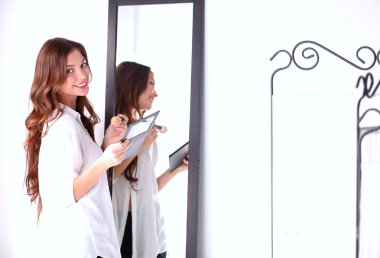 Genç ve güzel bir kadın aynanın yanında makyaj yapıyor.