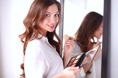 Genç ve güzel bir kadın aynanın yanında makyaj yapıyor.