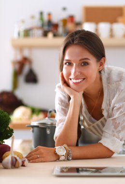 Mutfakta yemek yapmak için tablet bilgisayar kullanan genç bir kadın.