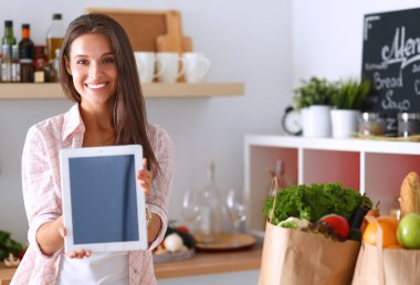 Mutfakta yemek yapmak için tablet bilgisayar kullanan genç bir kadın.