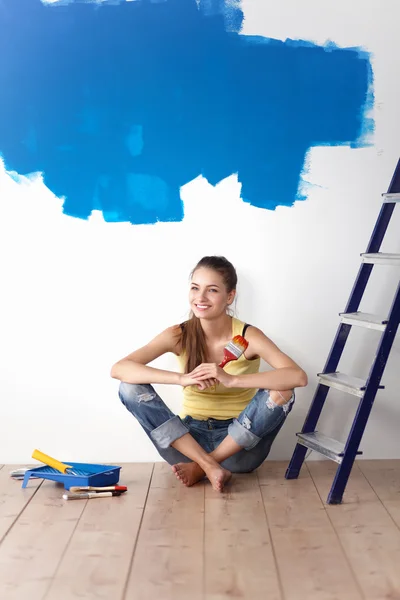 Portret malarza kobieta siedzi na podłodze w pobliżu ściany po malowaniu. — Zdjęcie stockowe