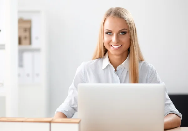 Attractive businesswoman sitting on a desk with laptop in the office — Stock Photo, Image