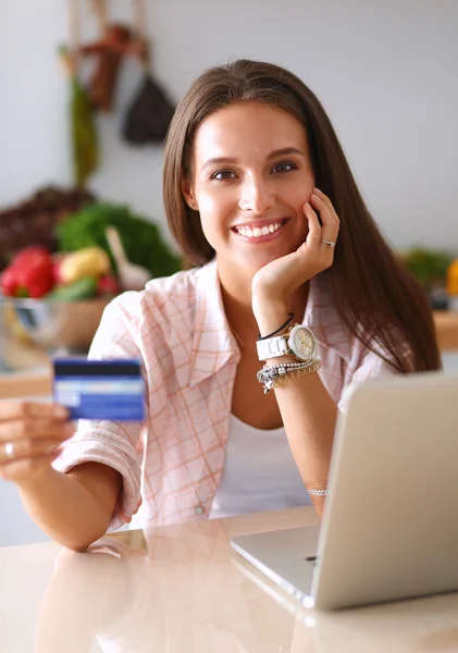 Mujer sonriente compras en línea utilizando la tableta y la tarjeta de crédito en la cocina —  Fotos de Stock